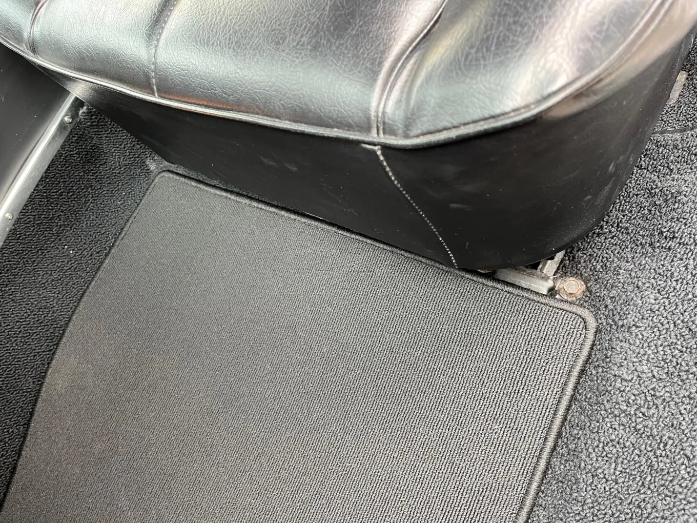 Blick in den Beifahrerfußraum eines Buick Riviera 1964. Dort liegt eine graue Fußmatte.