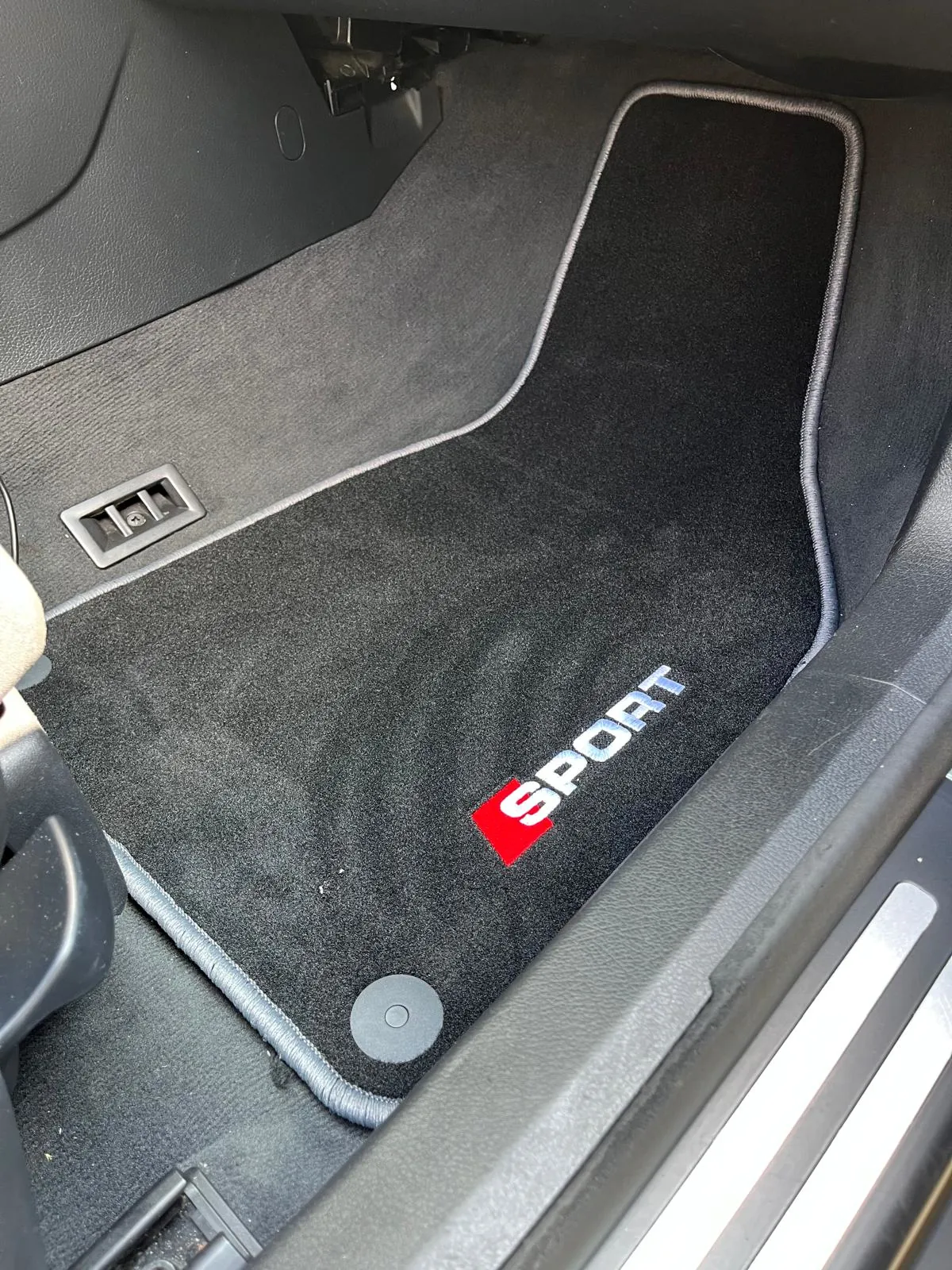 Blick in den Beifahrerfußraum eines Audi A4 8H Cabriolets. Hier liegt eine Fußmatte mit dem Stick "Sport".