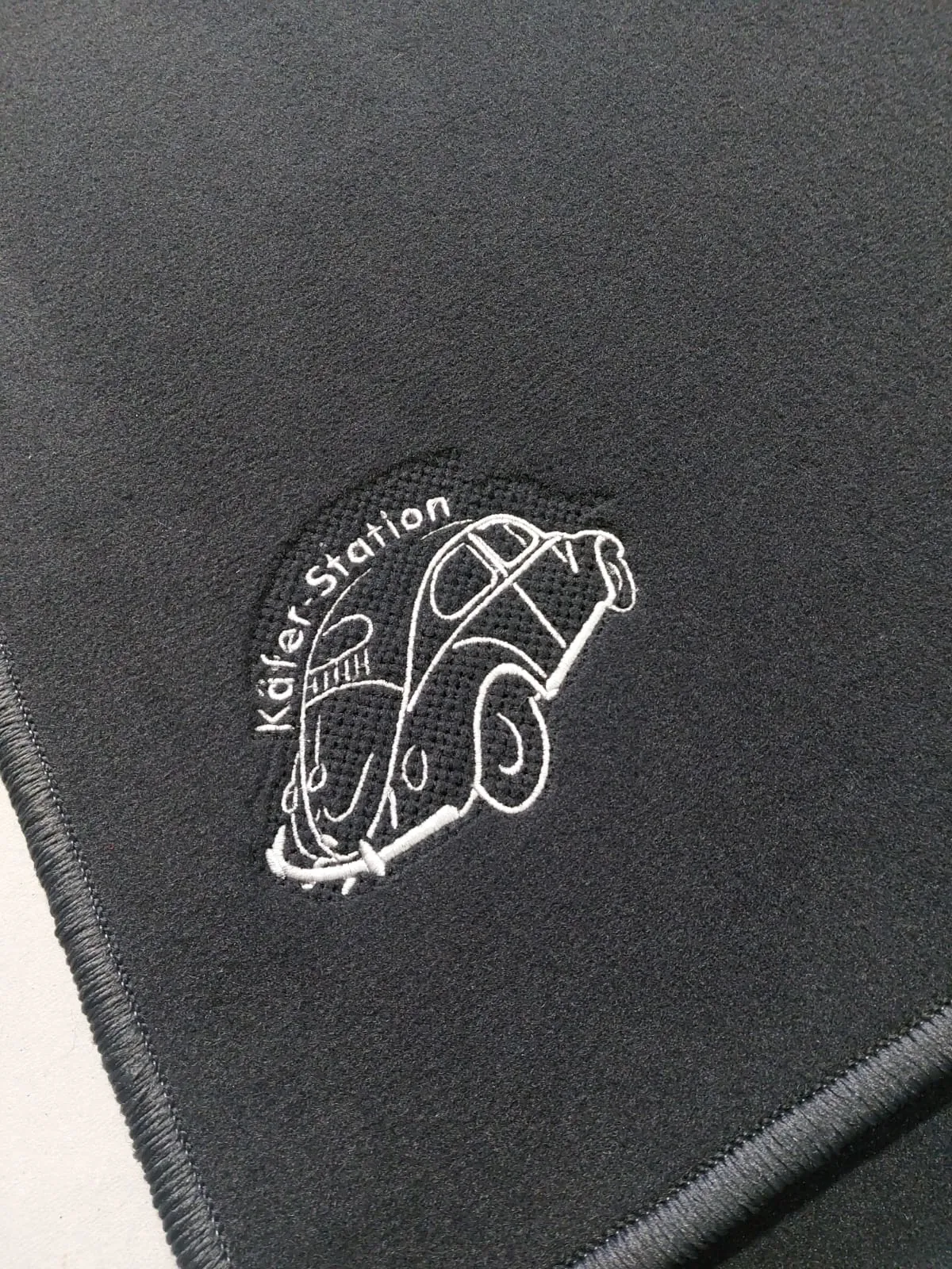 Eine Fußmatte mit der Aufdruck eines VW Käfers und „Käfer Station“ Schriftzug