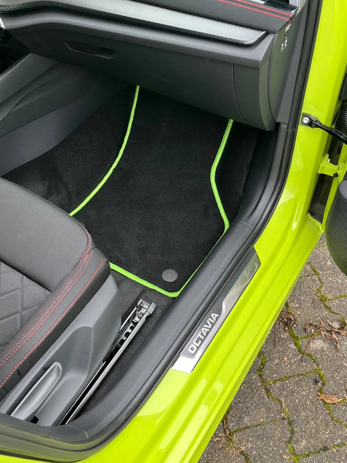 Blick in den Beifahrerfußraum eines Skoda Octavia 4 RS, in dem eine schwarze Fußmatte mit neon-grünem Rand liegt