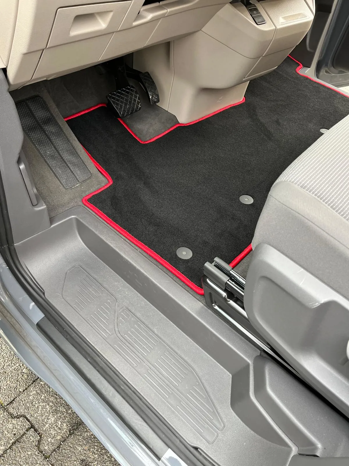 Blick in die Fahrerkabine eines VW T7 New Multivan 5, in der eine schwarze, perfekt eingepasste Fußbodenmatte mit rotem Rand liegt