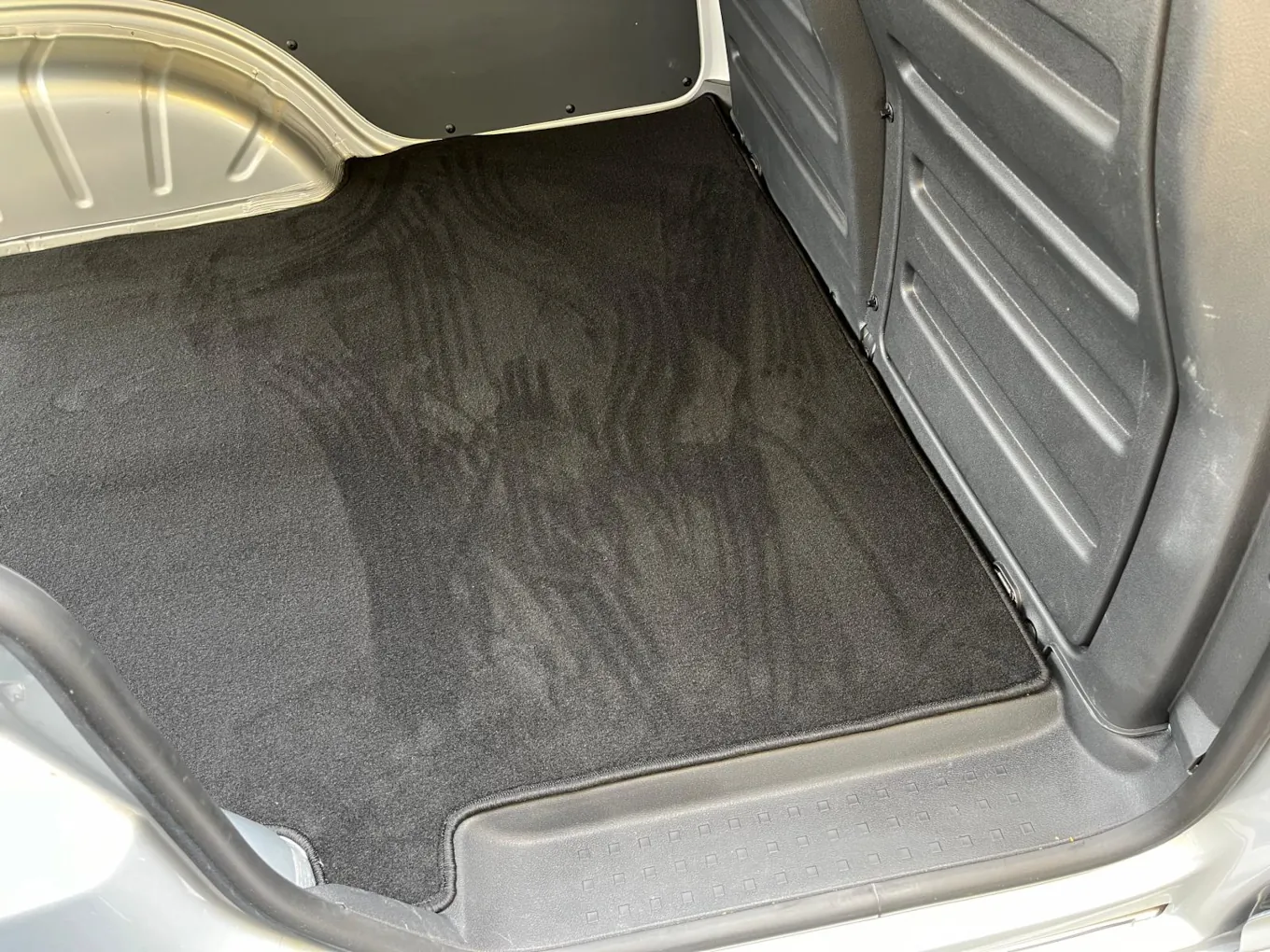 Blick durch die Seitentür in den Laderaum eines VW Caddy, dessen Boden mit einer schwarzen Laderaumschutzmatte verkleidet ist.
